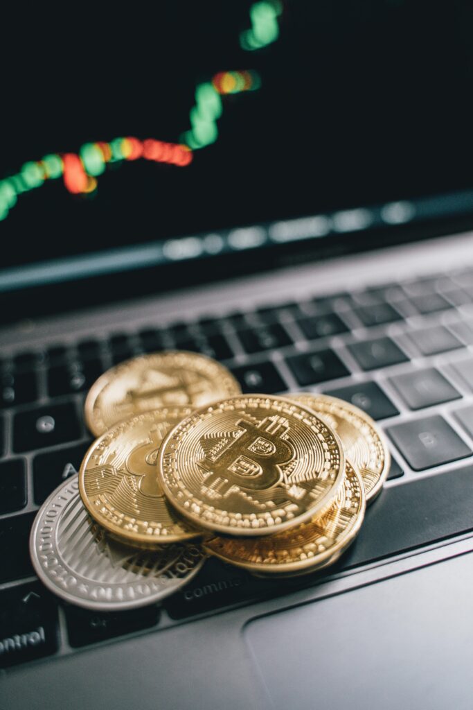 Stack of Bitcoin coins on a laptop keyboard with trading graph background, symbolizing cryptocurrency trading.
